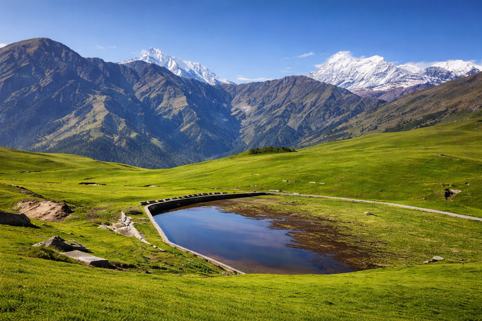 Ali Bedni Bugyal alpine meadow with green grassland, water pond and light snow covered Himalayan mountains under blue sky
