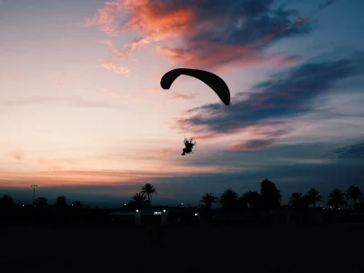A horizontal shot of a beach with a person gliding down on a paramotor parachute