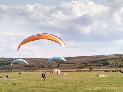 Paragliders silhouette flying over beautiful green landscape under blue sky with clouds. Paragliding school, practice